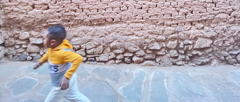 Child running in front of an earthen wall in ksar Amzrou (Zagora) southern Morocco