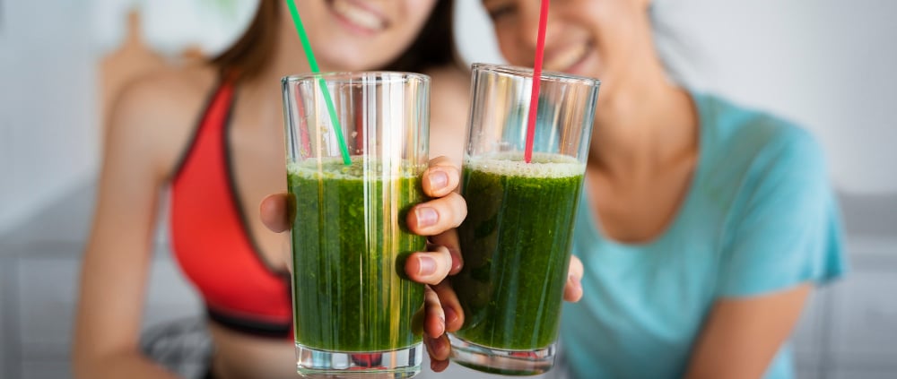 two women holding up two glasses of green juice