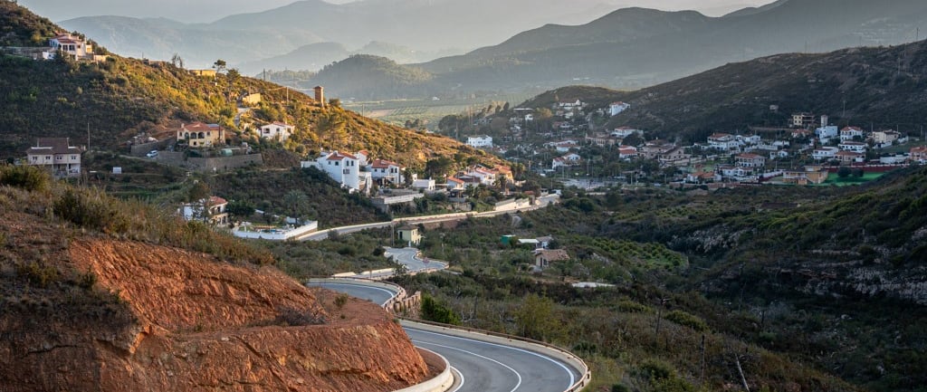 Winding road leading towards a Spanish mountain village and fading mountains in the background