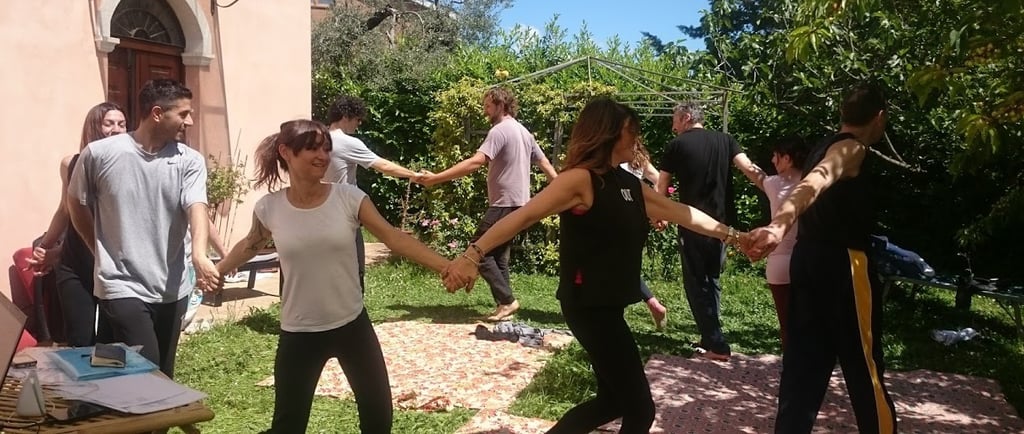 a group of people holding hands and dancing in a garden, classe di bioenergetica