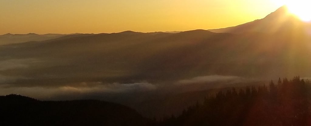 a person standing on a mountain top with a view of the sun setting