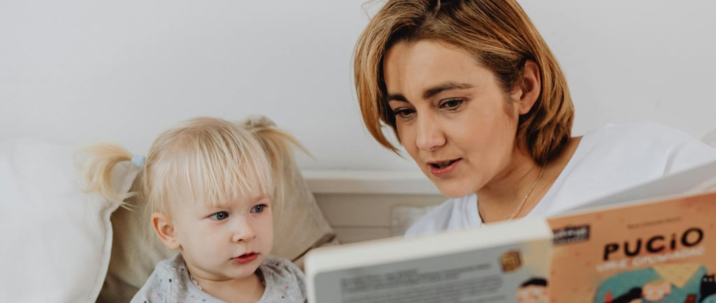 a woman reading a book to her daughter while sitting on a bed