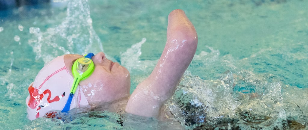 Young girl swimming on her back in pink swim cap with flamingos and blue and green goggles