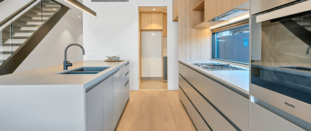Modern kitchen with sleek cabinetry, built-in appliances, and under-stair sink area