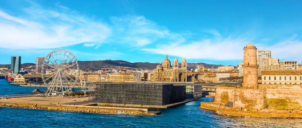 Cidade de Marselha vista do mar, com fortalezas e a grande roda-gigante na chegada ao porto