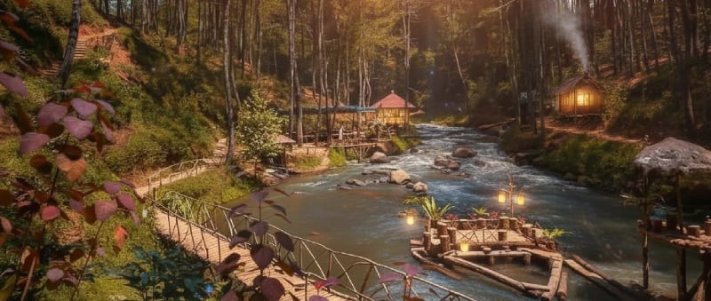 Sebuah jembatan kayu melintasi sungai yang mengalir di hutan pinus yang rimbun, dengan pondok-pondok di tepi sungai, di bawah