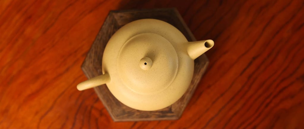 An overhead view of a yellow teapot placed on a wooden stand