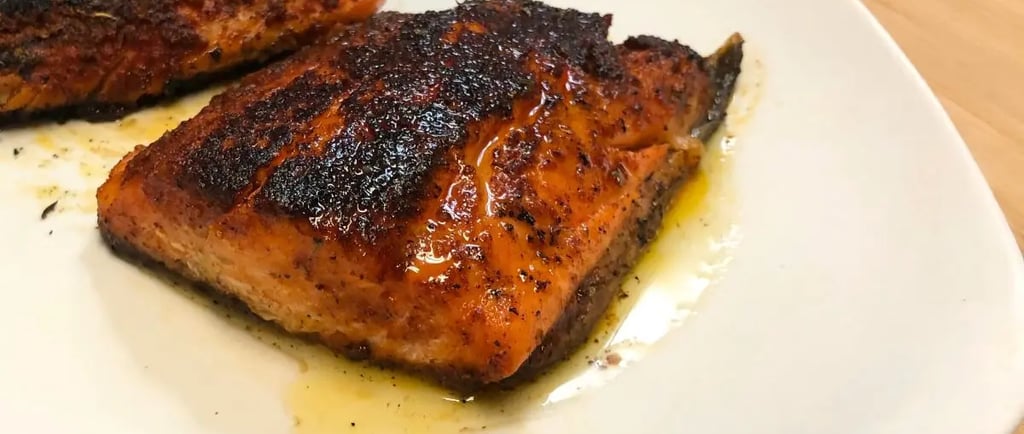 Blackened steelhead trout on a white plate topped with lemon garlic butter sauce