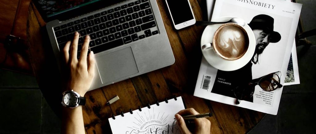 a person sitting at a table with a laptop, a notebook and coffee