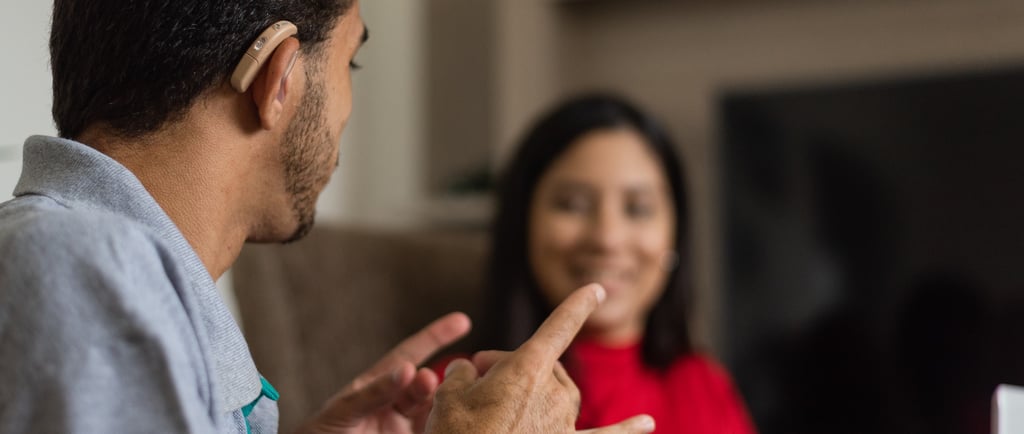 a deaf interpreter with a hearing aid in signing to someone on the couch