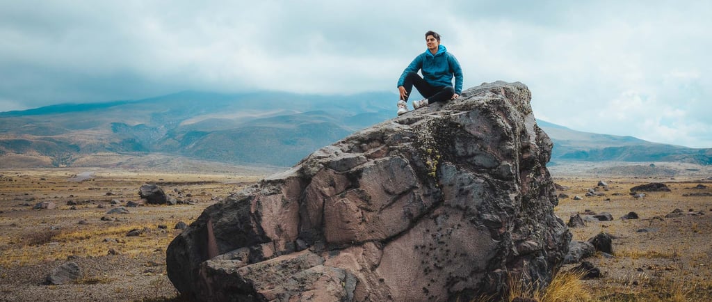 Fotografía de retrato profesional de aventura de un joven sentado en la cima de una roca en un paisaje hermoso de montaña