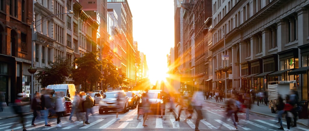 a busy city with traffic and pedestrians, and a bright sun setting in the background