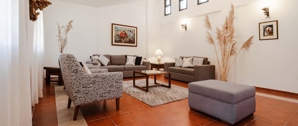 Habitación interior amoblada y decorada con pinturas, candelabro plantas con sillones cafés AirBnB en Quito, Ecuador