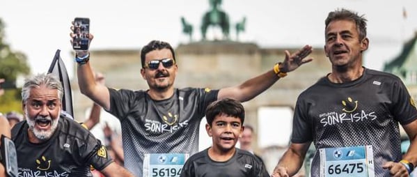 Cuatro corredores de Empujando Sonrisas corren eufóricos con la Puerta de Brandenburgo de fondo