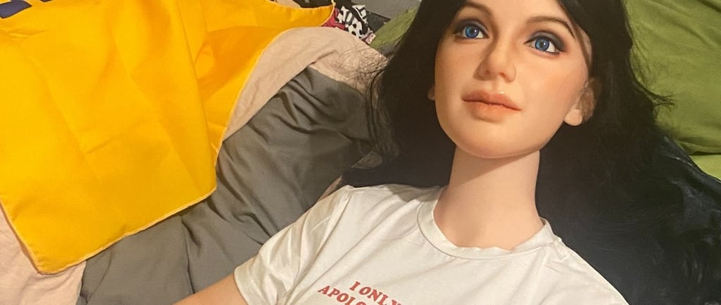 a sex doll posed in bed covered by a blanket