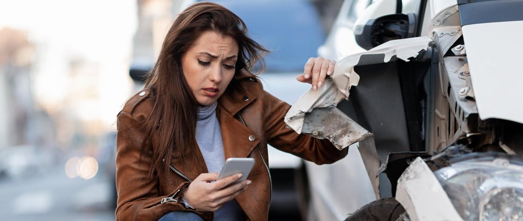 a woman in a leather jacket is looking at her phone phone after having a car crash
