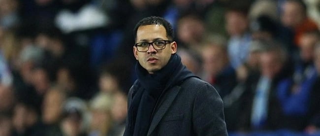 a man in a black coat and glasses on a soccer field