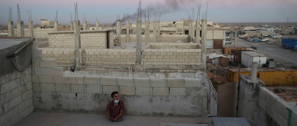 A child sits alone on a rooftop in a conflict zone, symbolizing the personal impact of forced migration and the resilience of