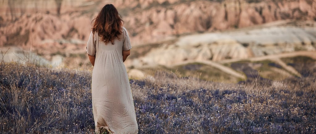 Woman in a beige dress standing in a lavender field with Cappadocia’s rock formations in the background