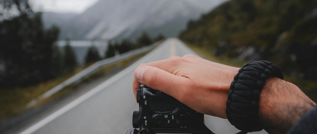 a person holding a camera taking a picture of a vast open road in the mountains
