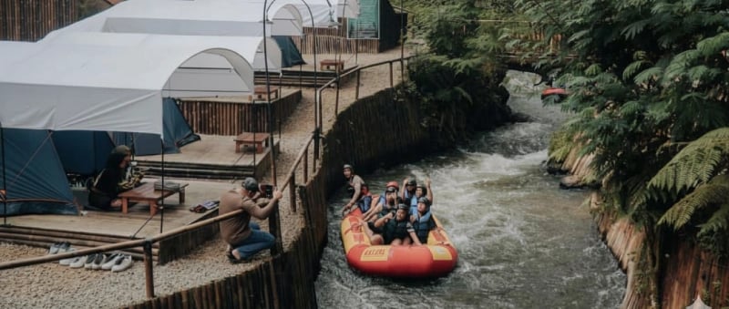 Rombongan rafting di sungai Pangalengan dekat tenda camping riverside, menyorot petualangan dan penginapan alam.