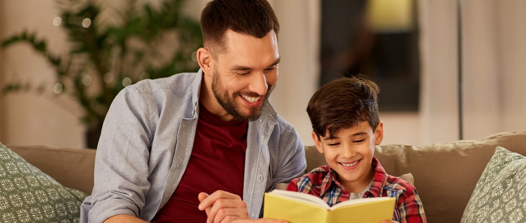 father and son are sitting on a couch reading a book