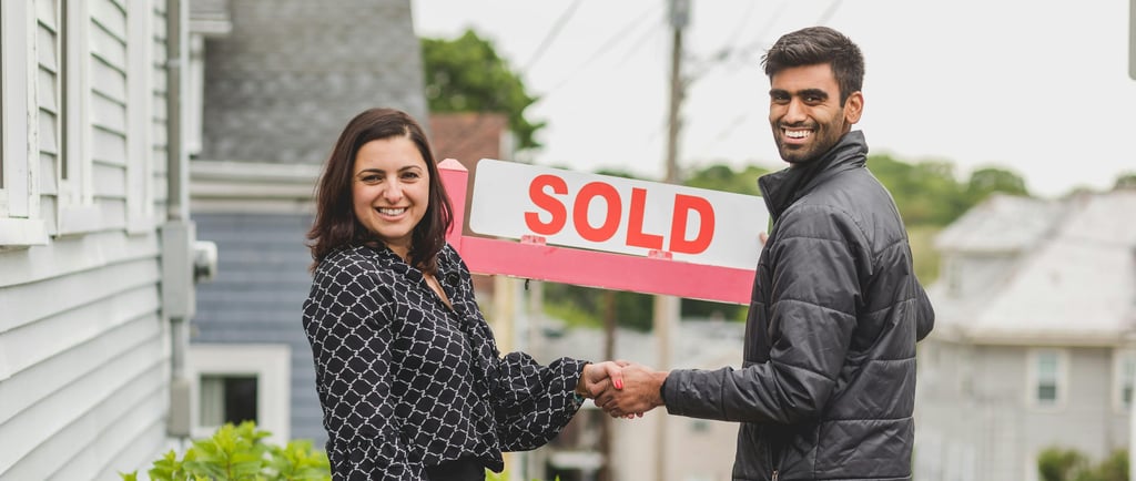 First Time home Buyer in Clagary. A man and woman shaking hands in front of a sold sign