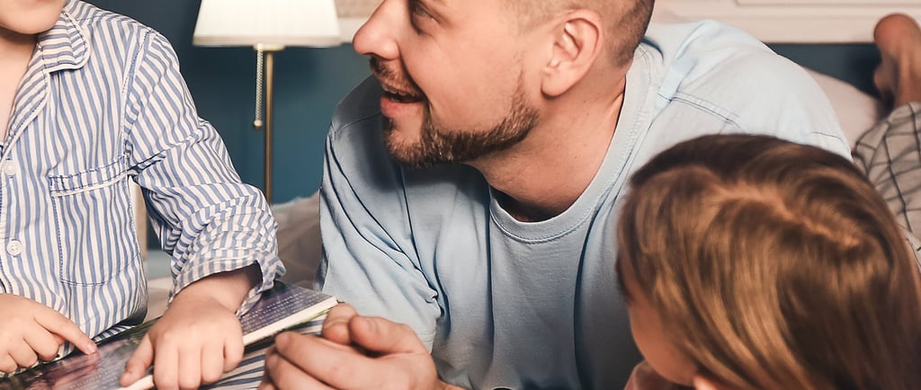 a father and two children are laying on a bed reading a book