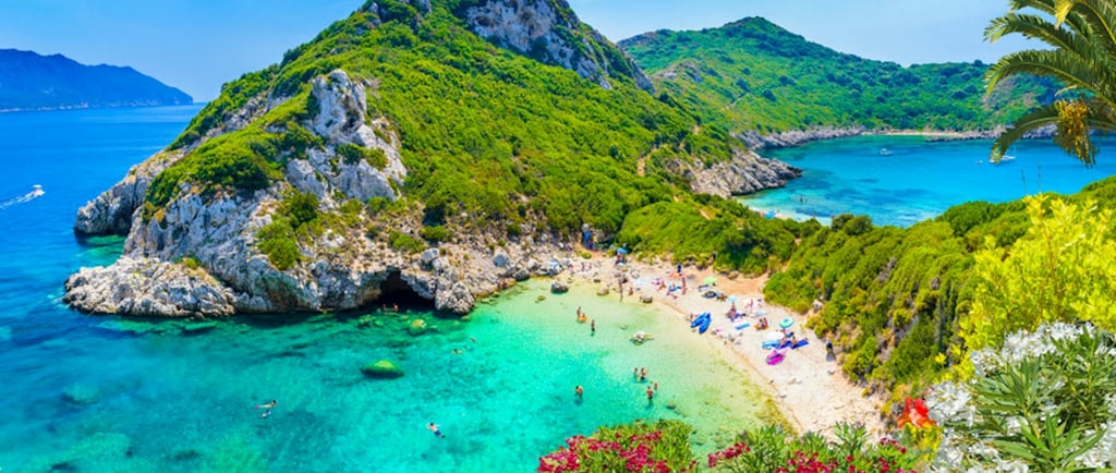 Panoramic view of  Rovinia beach in Corfu, Greece, with turquoise waters and lush green cliffs.
