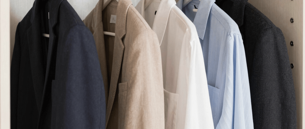 Organized wooden wardrobe with blazers and button-up shirts hanging on a metal rod.