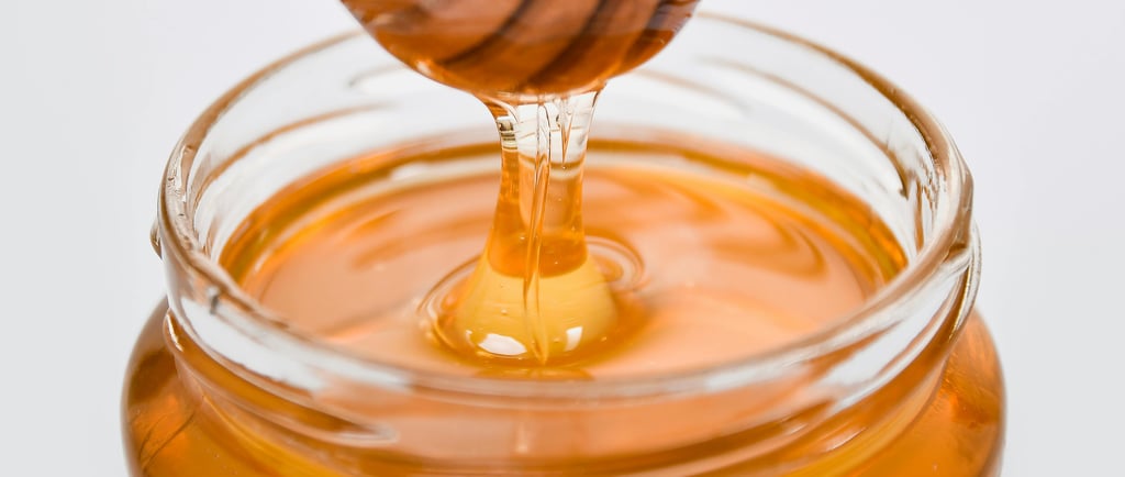 Jar of Manuka honey on a clean, minimalist kitchen counter with a wooden honey dipper.