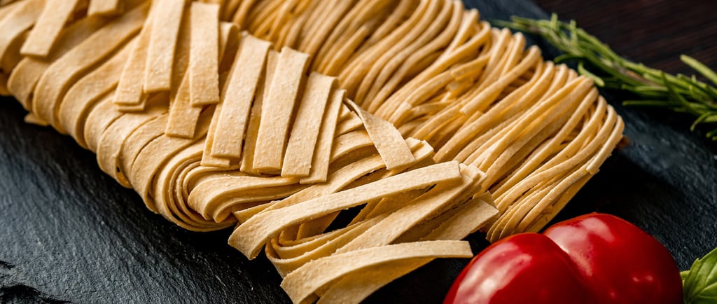 Frische hausgemachte Fettuccine auf schwarzem Schiefer mit Cherrytomaten und Basilikum.
