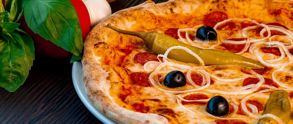 Heiße Pepperoni-Pizza mit schwarzen Oliven, Zwiebeln und grünen Paprika neben frischen Basilikumblät