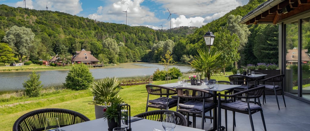 Outdoor-Seeterrasse mit moderner Möblierung und Blick auf ein Tal mit Windrädern.