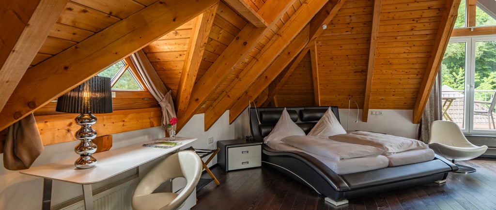 Modernes Hotelzimmer im Dachgeschoss mit gewölbter Holzdecke, Lederbett und stilvollem Arbeitsplatz