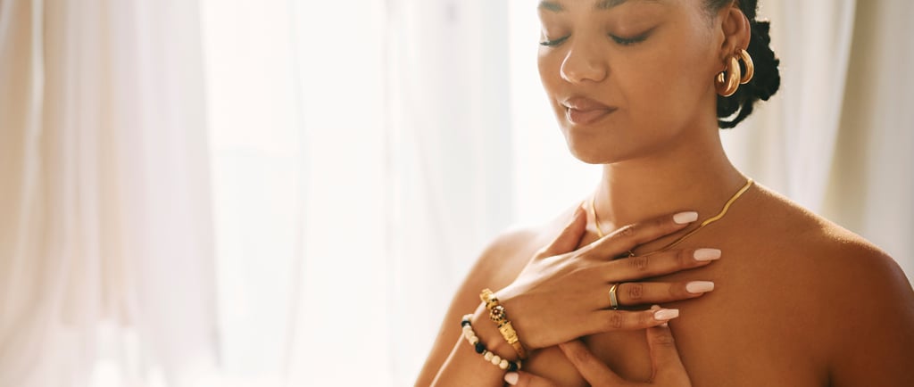 Uma mulher serena, usando joias de ouro, pratica meditação mindfulness com as mãos sobre o peito.