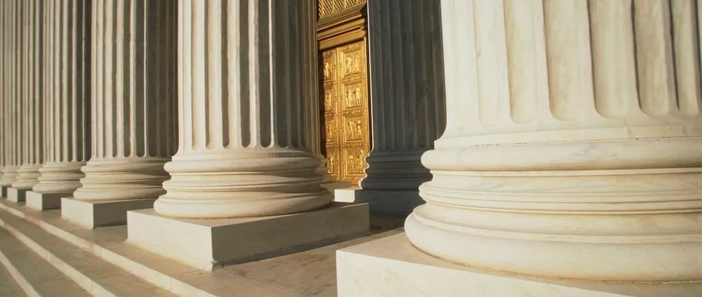 White marble fluted columns of a neoclassical building leading to an ornate golden door.