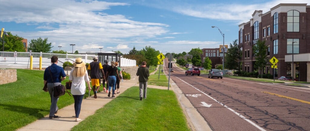 People walking on a sidewalk next to a street with a painted bike lane