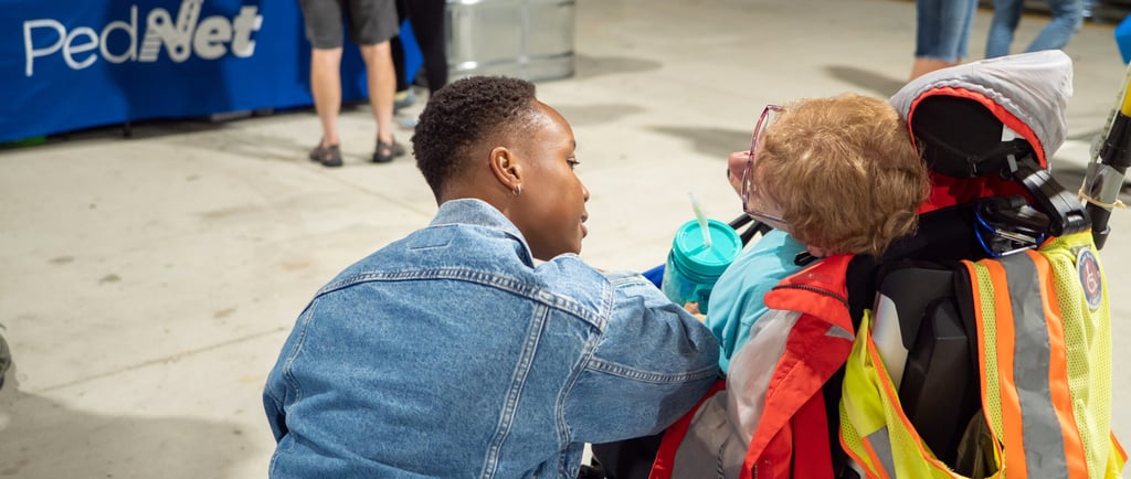 Photo of a person in an automated wheelchair speaking with someone hovering near them.