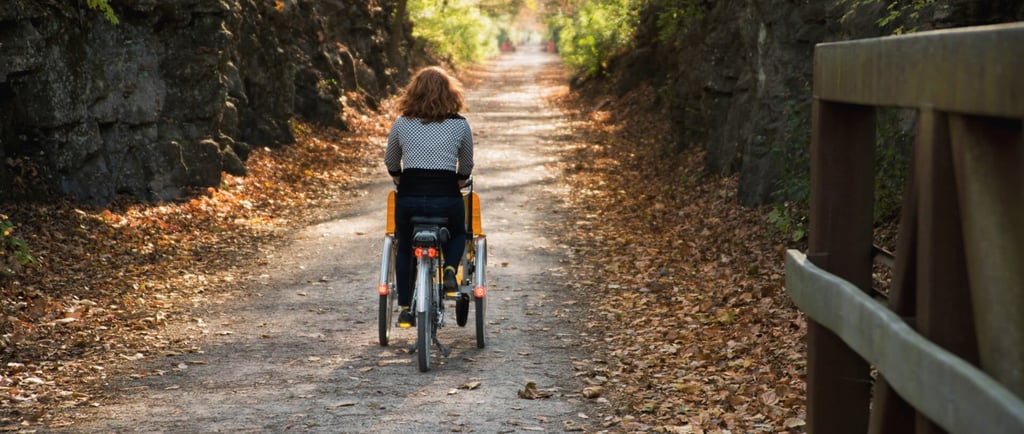 A woman with shoulder length red hair rides a three-wheeled wheelchair bike away from the camera.