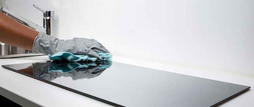 Une personne nettoyant la table de cuisson avec un chiffon posé dessus.