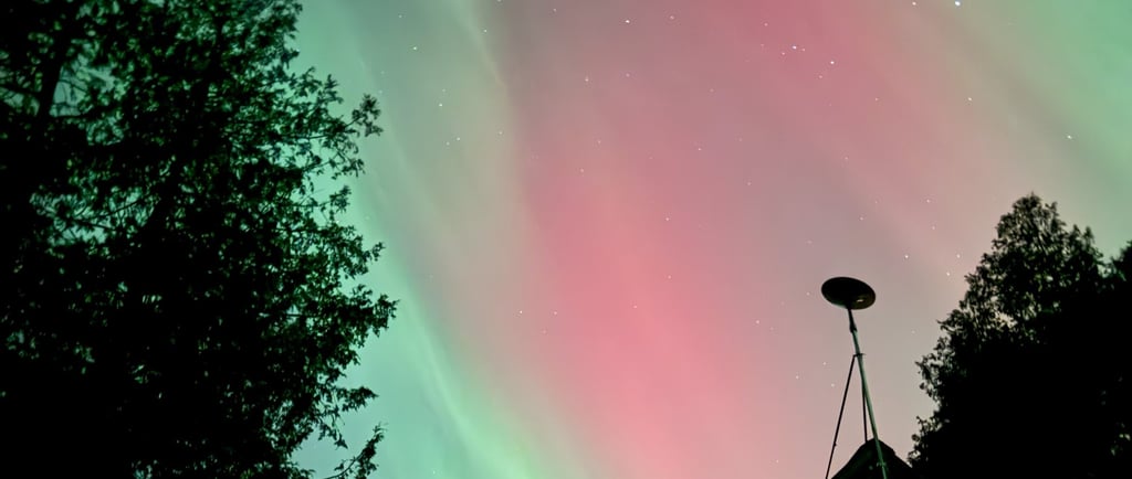 Green and pink northern lights with silhouette of a house with a satellite dish. Image by me.