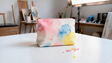 A close-up of a canvas cosmetic pouch with an Aquarelle watercolor effect, in an artist's studio.