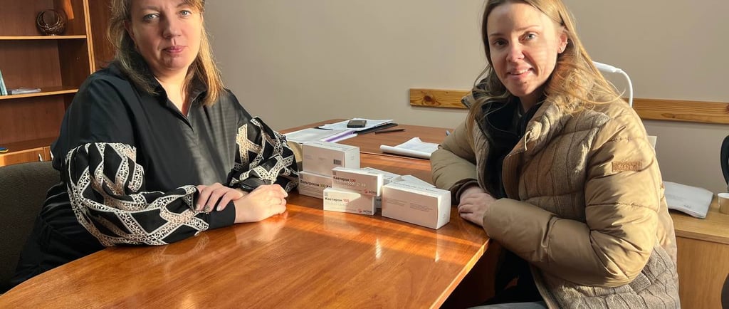 дві жінки сидять за столом з упаковками ліків