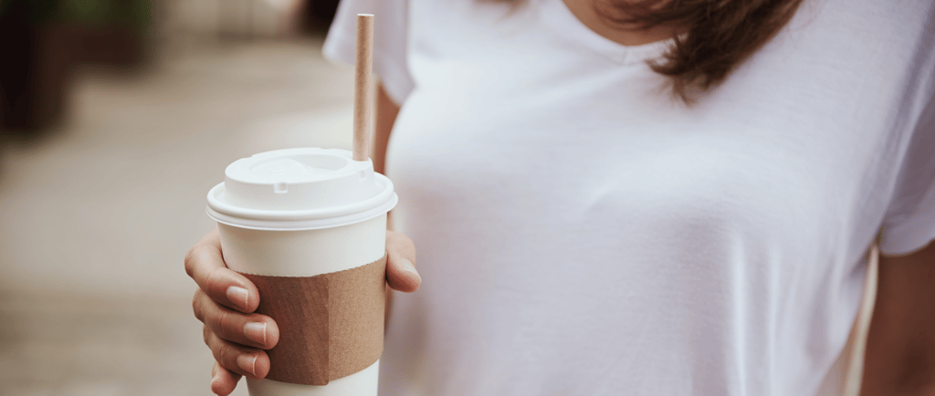Close-up of woman in white shirt holding takeaway coffee cup