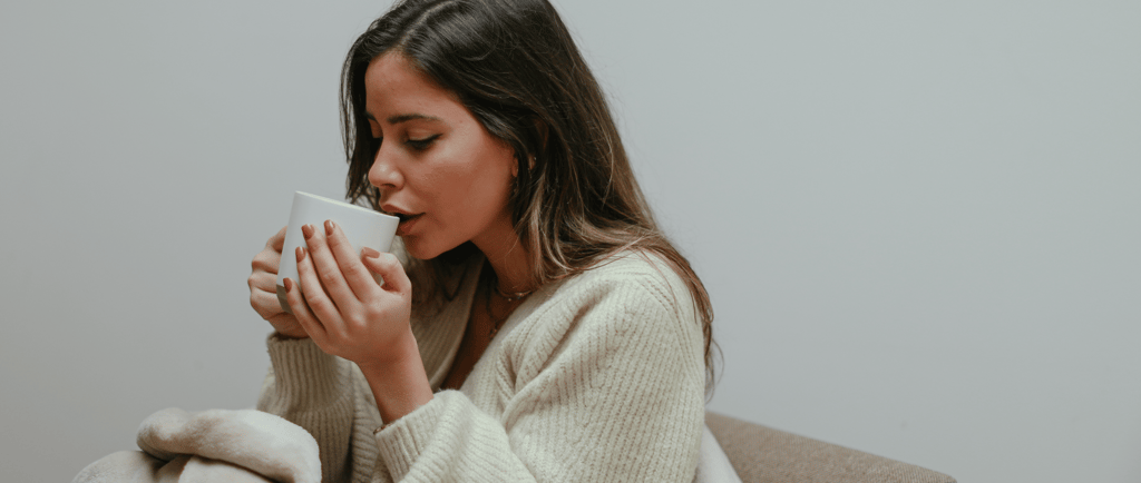 Woman wrapped in a cozy blanket holding a mug, sitting on a couch