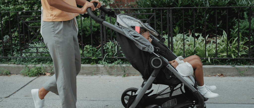 Parent pushing baby stroller outdoors on a sunny day