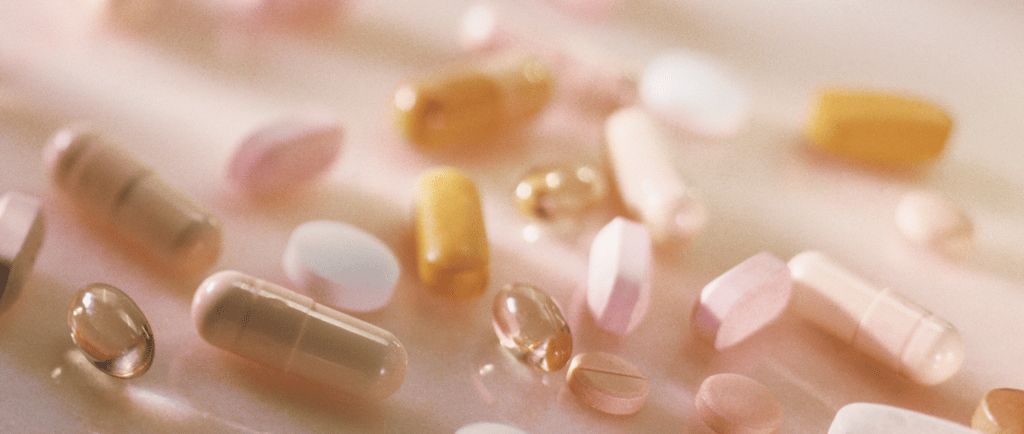 Close-up of assorted fertility supplements and capsules in soft, pinkish lighting.
