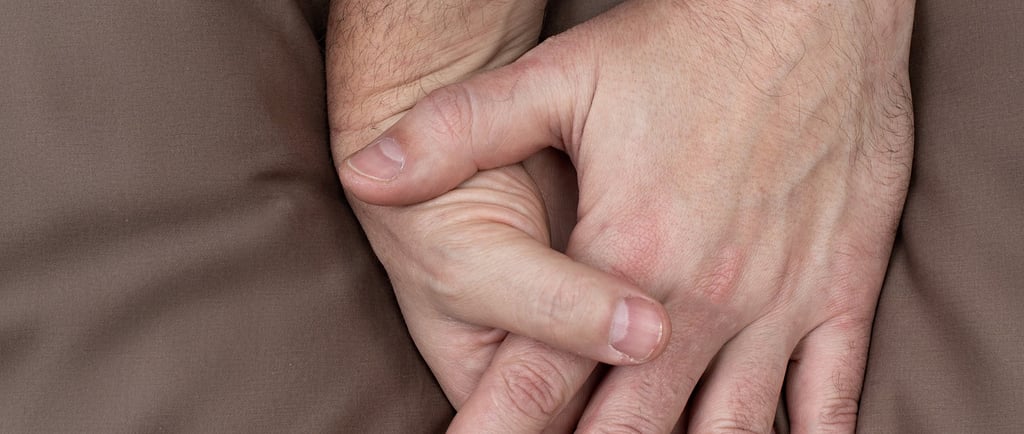 Two male hands entwined together on top of bedsheets