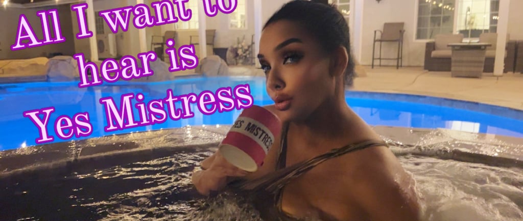 MsMadyson in a chocolate swimsuit in a hot tube at night holding a pink cup that says Yes Mistress